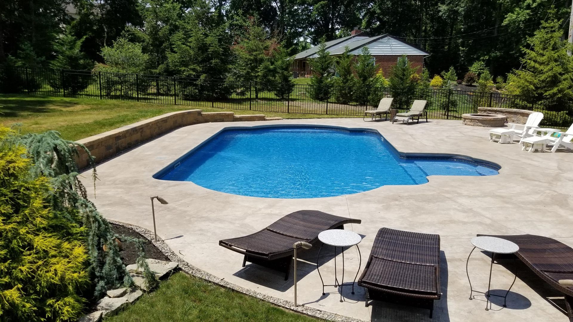 Backyard pool with lounge chairs on concrete patio; green grass and trees in background.