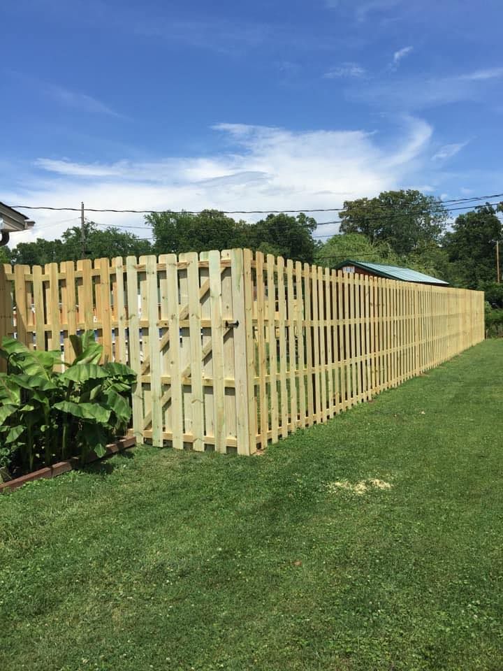 A newly installed light wood fence bordering a green lawn under a bright blue sky.