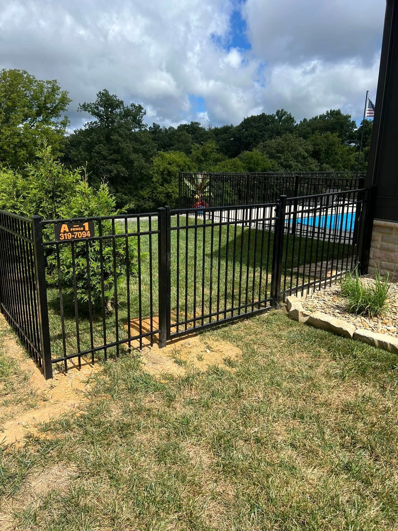 A black metal fence encloses a pool area in a backyard, with a small caution sign attached to one of the panels.