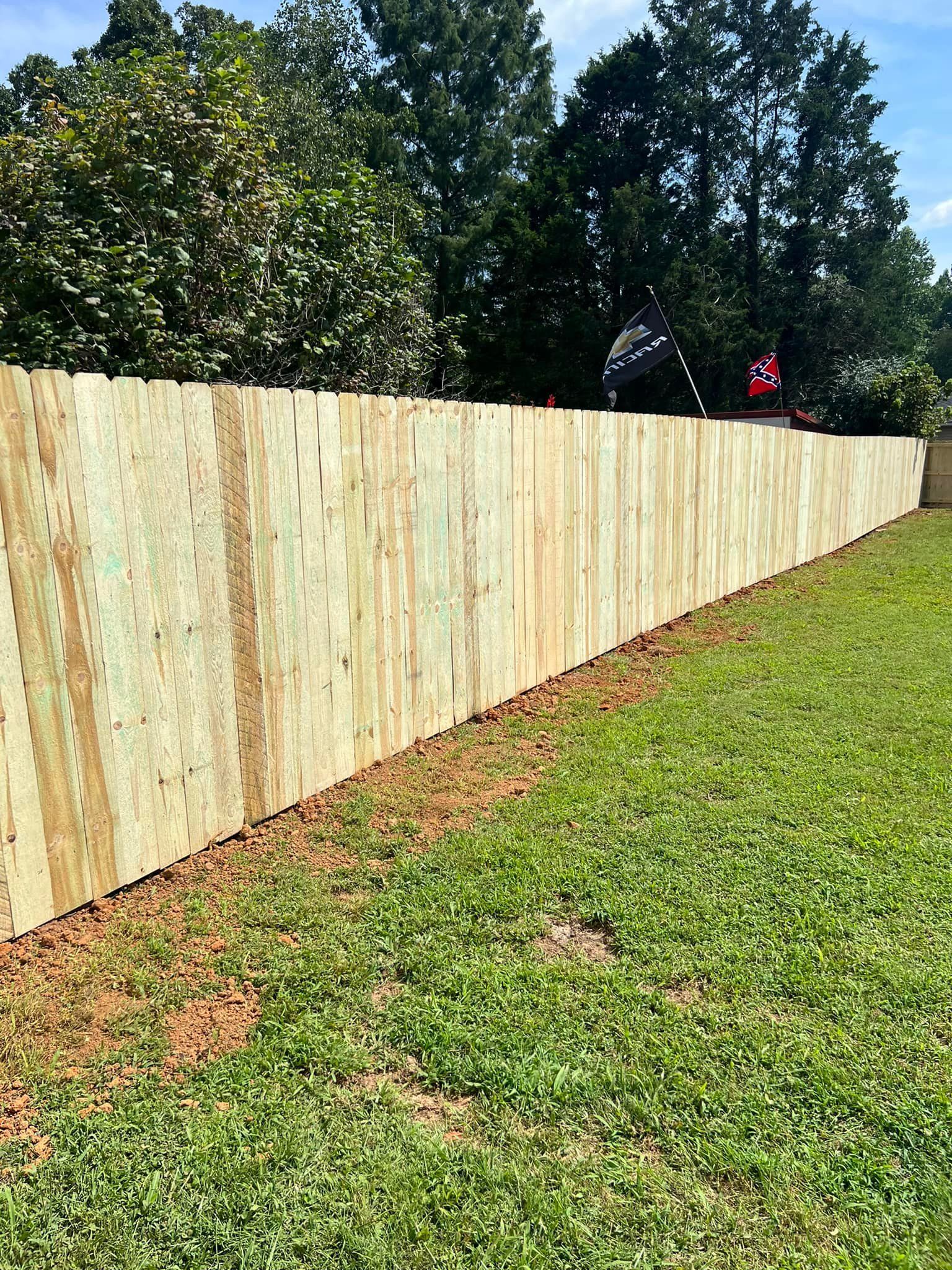 A new, light-colored wooden fence runs along the edge of a green lawn under a sunny sky.