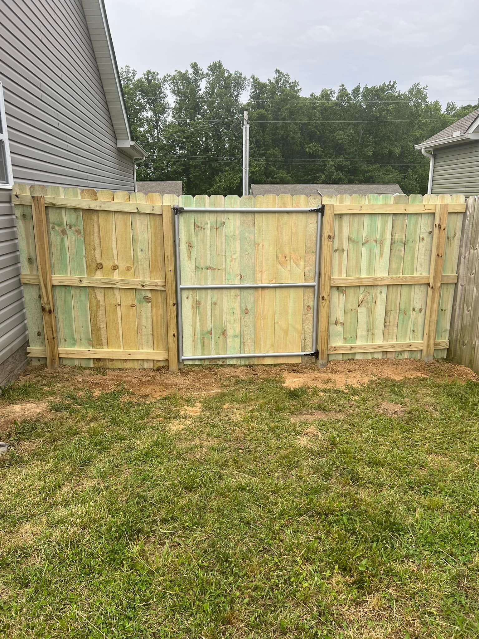 A new wood privacy fence featuring a metal-framed gate in a backyard setting.