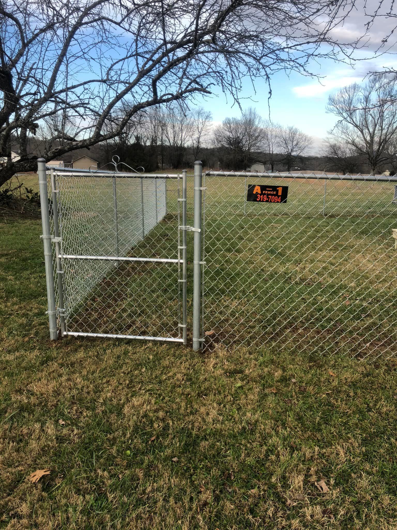 A chain-link fence gate stands in a grassy field with a small, black 