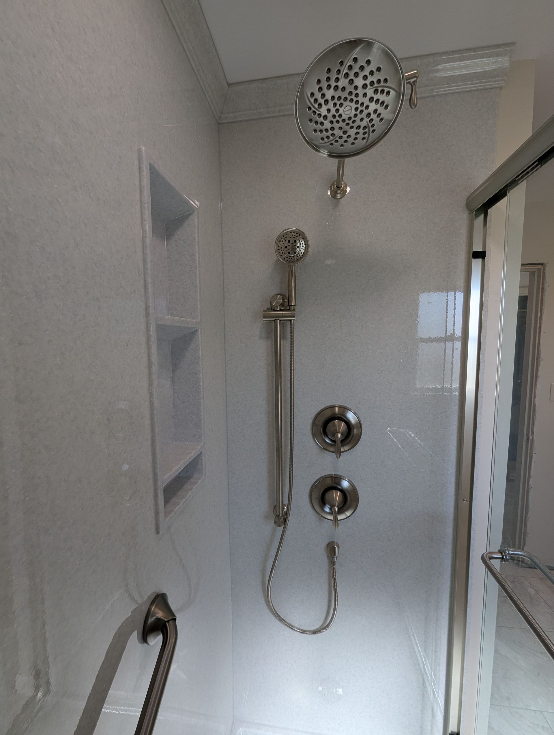 A shower with a shower head and a hand rail.