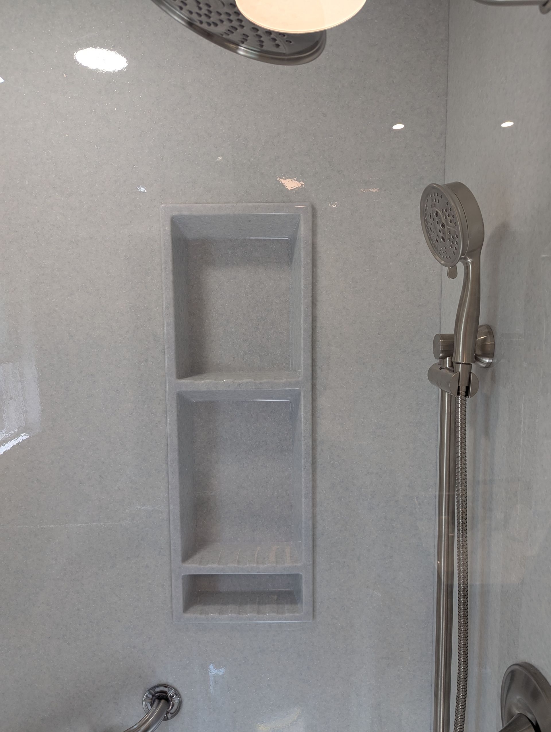 A shower with a shower head and a shelf on the wall.