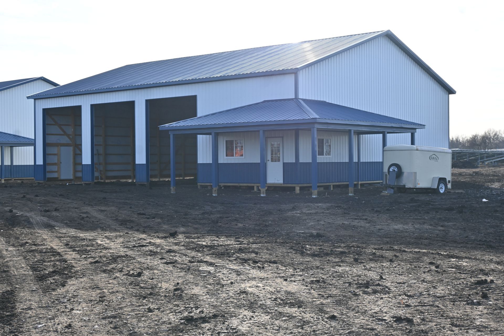 A white barn with a blue porch and a trailer in front of it