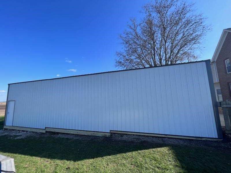 A large white building is sitting in the grass in front of a brick building.