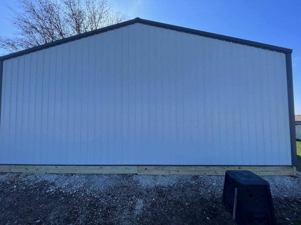 A white building with a black roof is sitting on top of a gravel lot.
