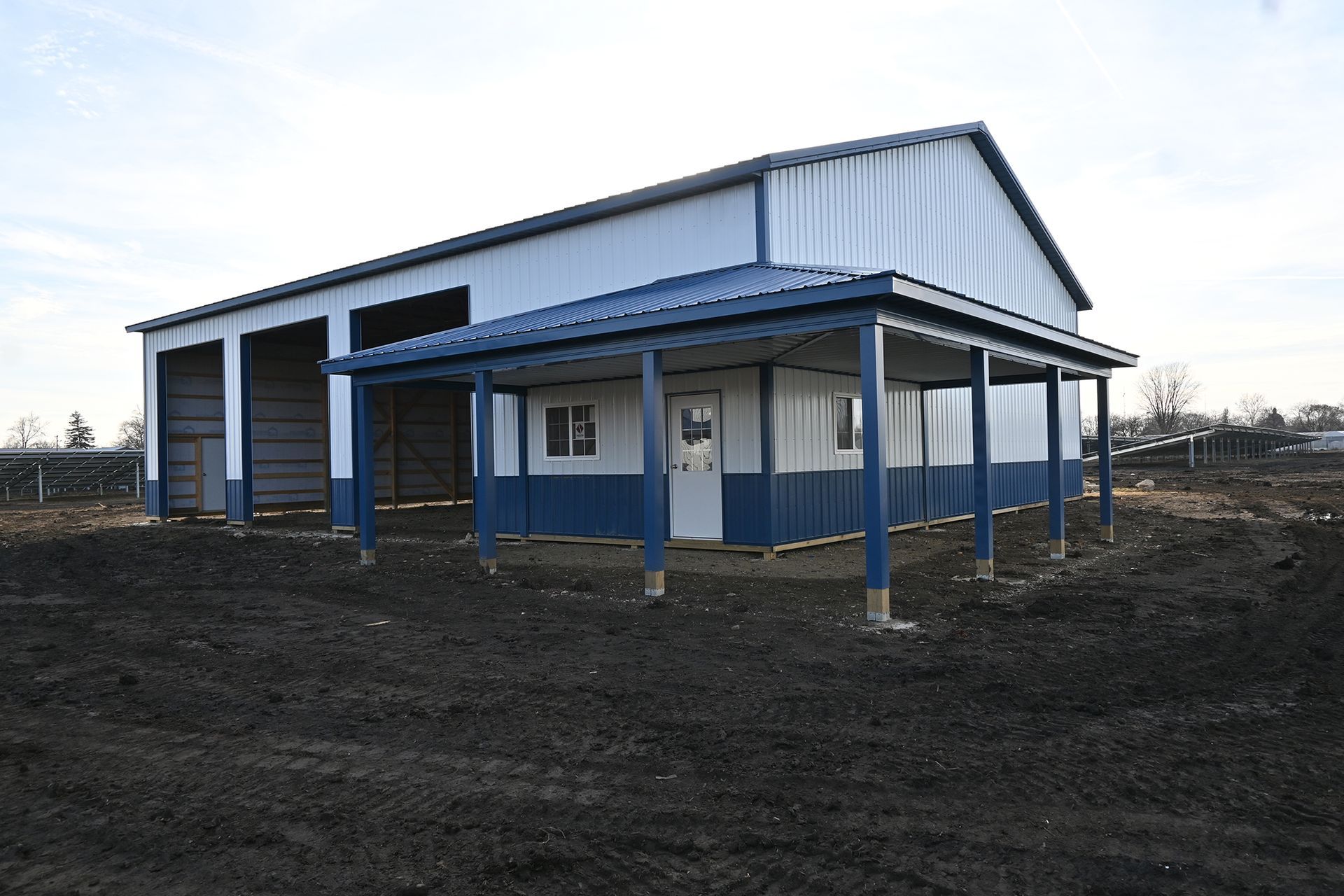 A white and blue building with a porch is sitting in the middle of a dirt field.