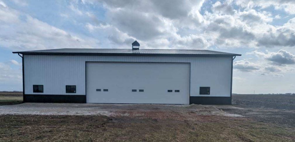 A white and black building with a large garage door is sitting in the middle of a field.
