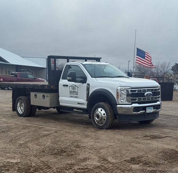 White flatbed truck parked on gravel lot with American flag in the background