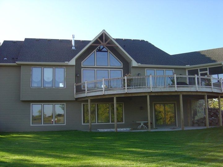 Large suburban house with a dark roof, curved balcony, and a green lawn in front.