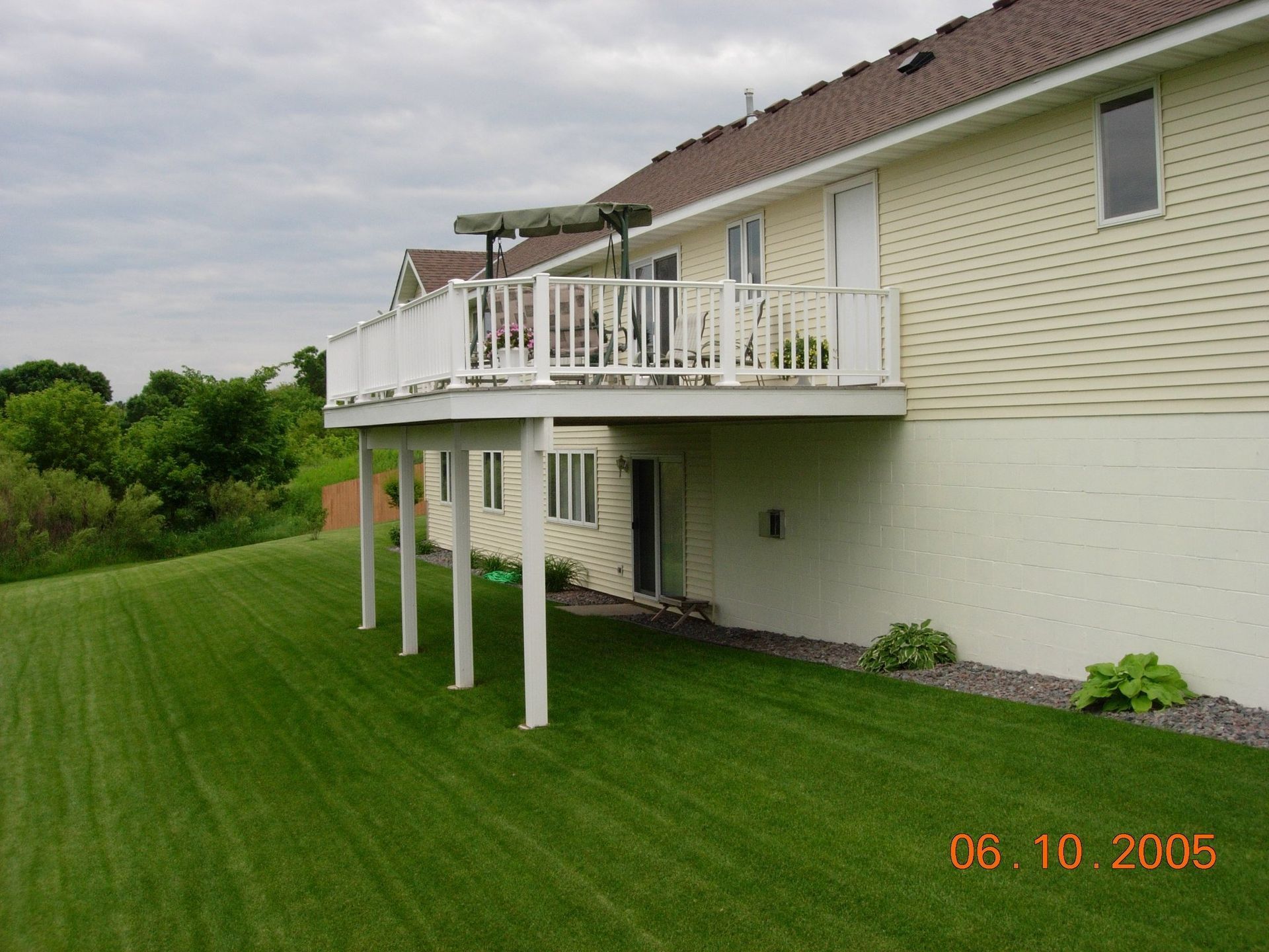 Suburban house with a raised deck and white support posts over a neatly mowed green lawn