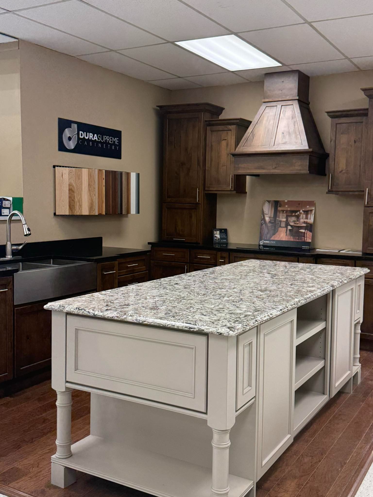 Kitchen showroom with a white island and speckled countertop, dark wood cabinets, and a range hood