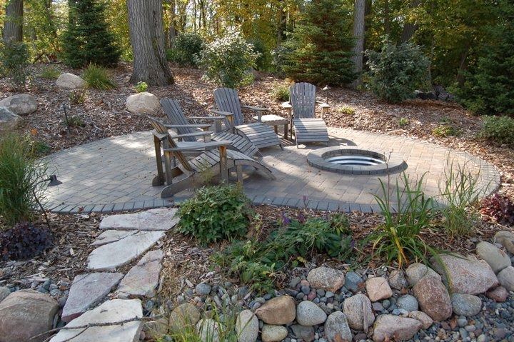 Stone patio with Adirondack chairs and a fire pit in a landscaped garden.