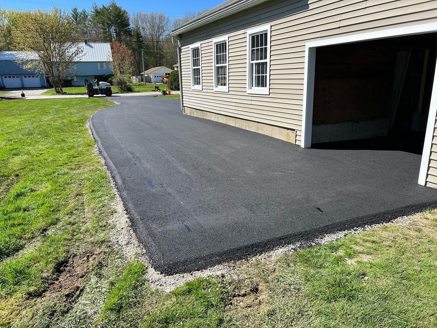 Newly paved asphalt driveway next to a garage, bordered by grass and gravel.