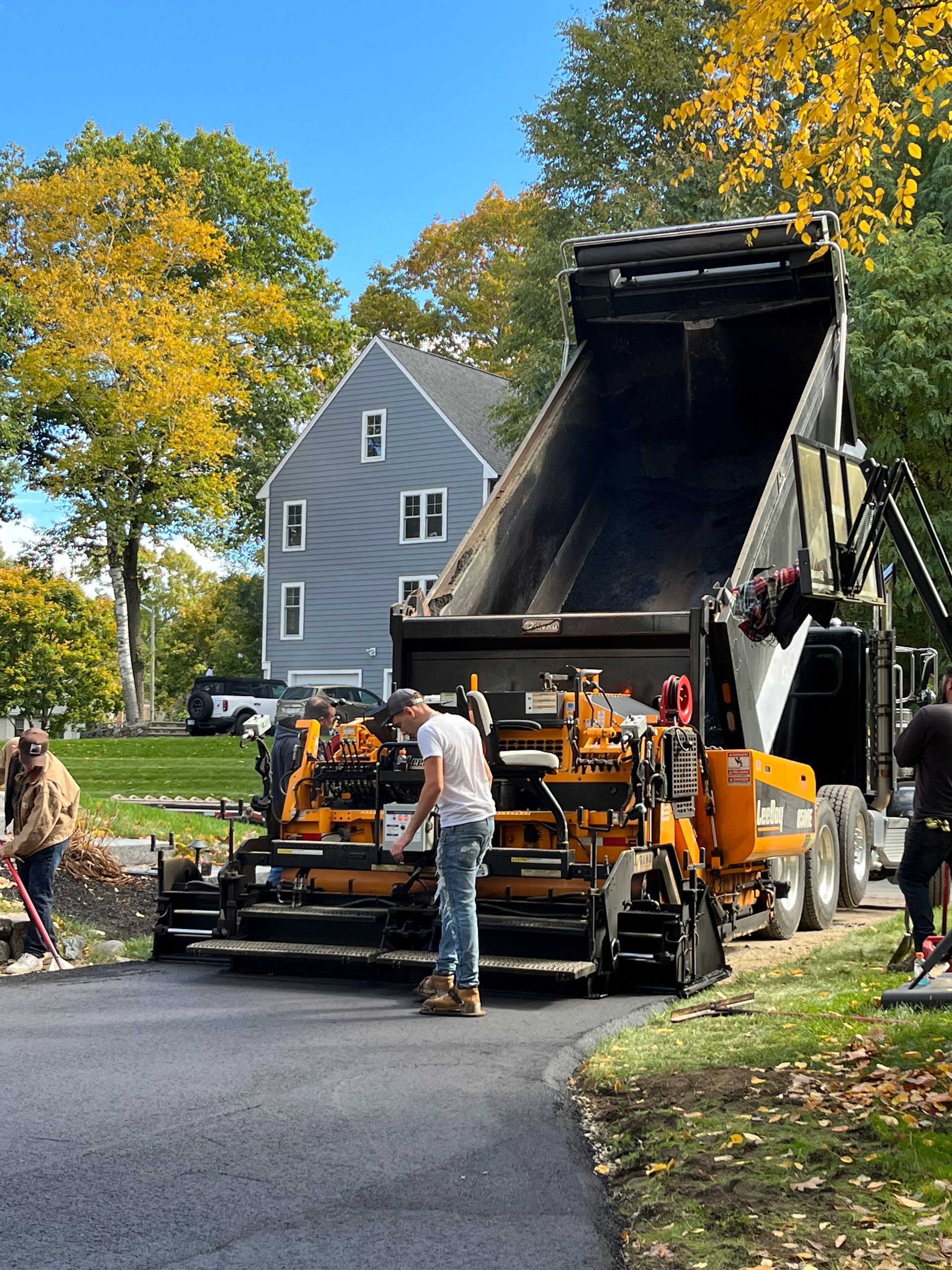 Asphalt paving crew at work; dump truck unloading asphalt into a paving machine.