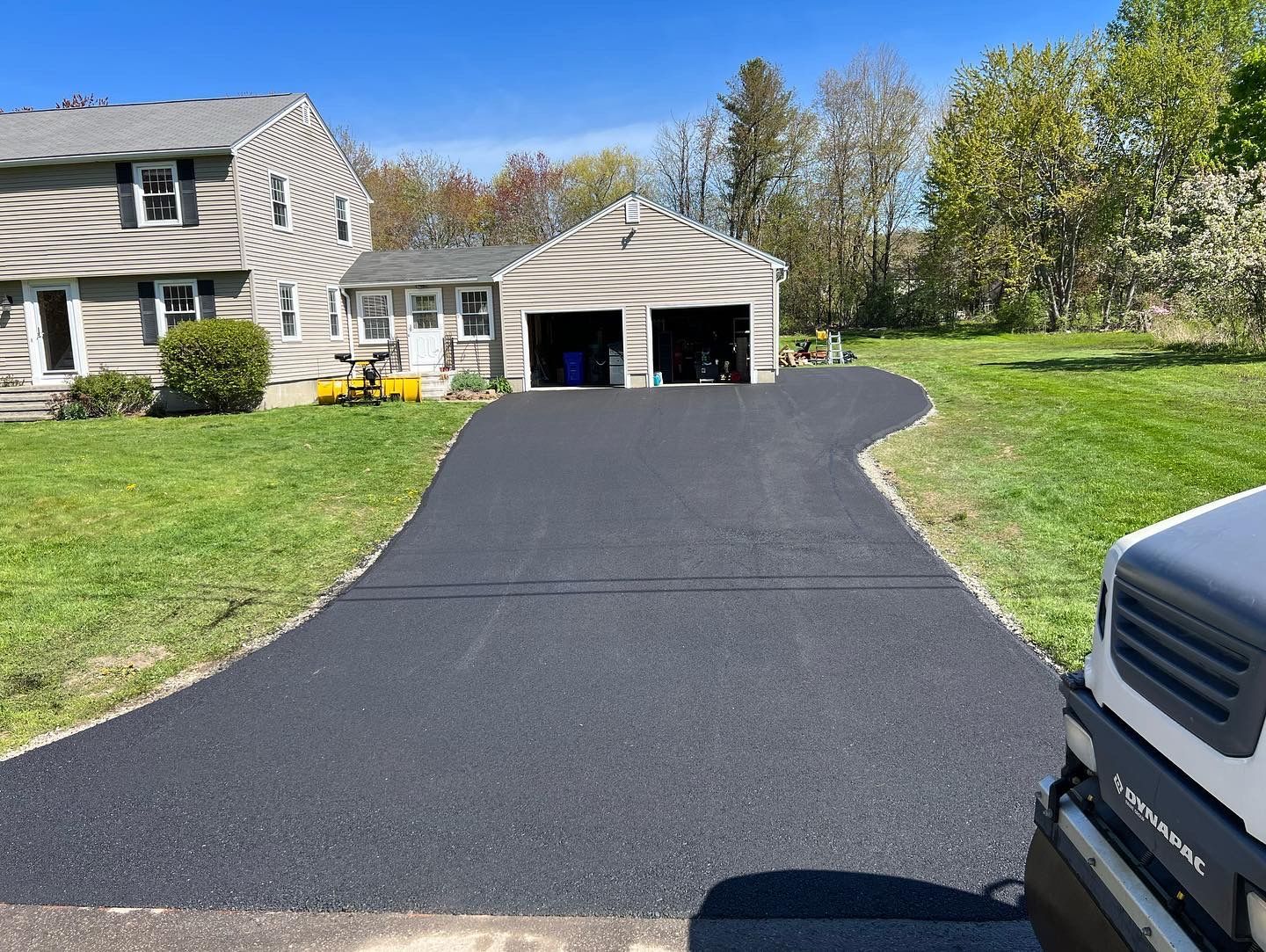 Black asphalt driveway leads to a two-car garage, flanked by green grass and a house.