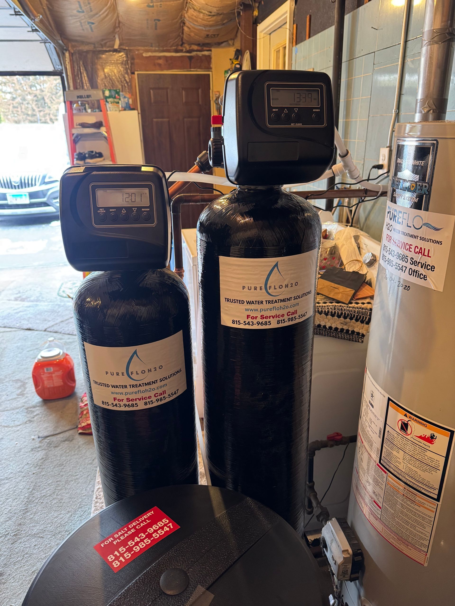 Two black water filtration systems with digital displays in a garage.