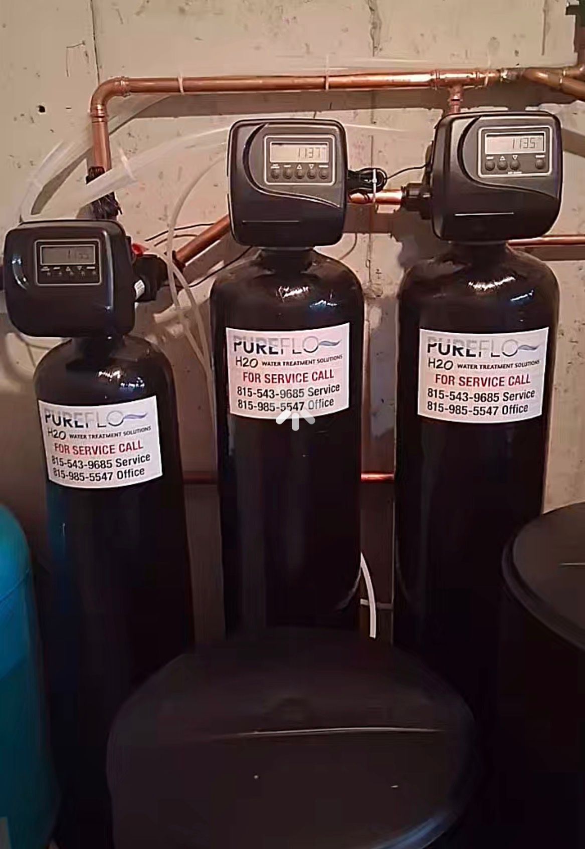 Three black water filtration tanks with digital meters, connected by copper pipes.