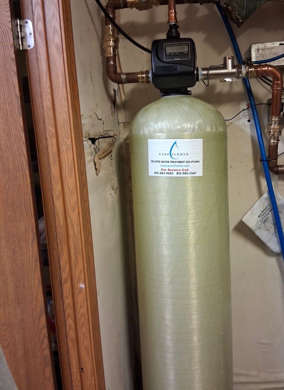 A large, beige water filtration tank with a digital control valve, installed indoors next to a wooden door frame. 