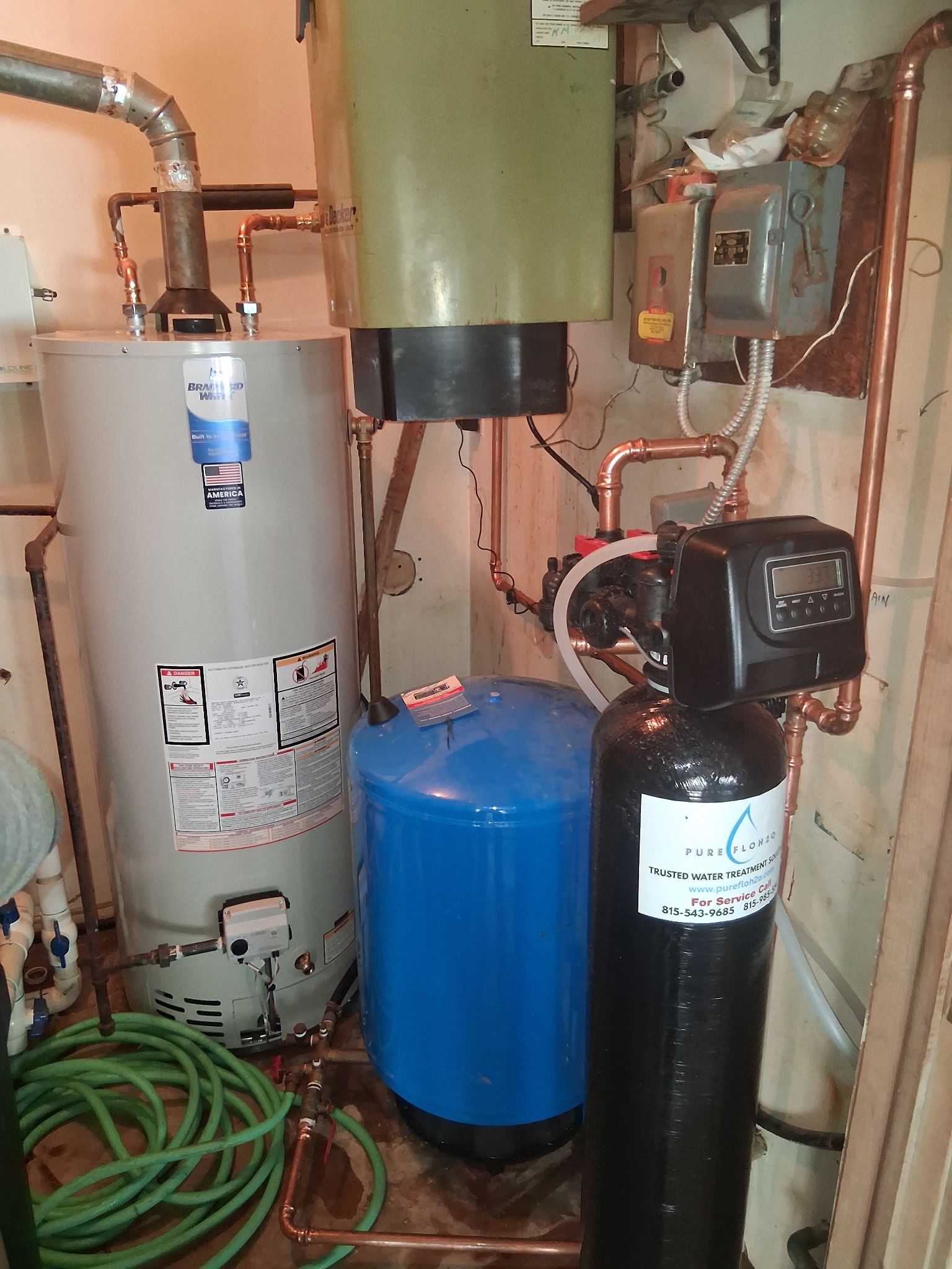 A water heater, blue pressure tank, and black water filtration unit connected by copper plumbing in a utility area. 