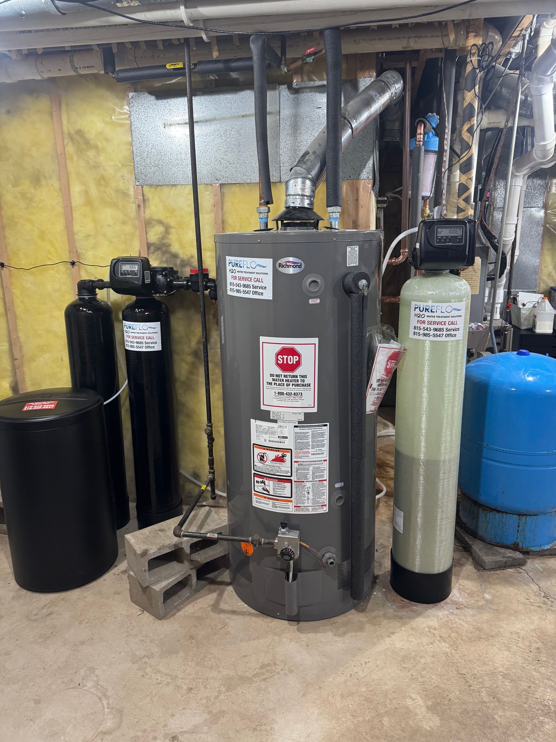 Water heater and filtration system in a basement. Grey tank, black and green cylinders, blue tank.