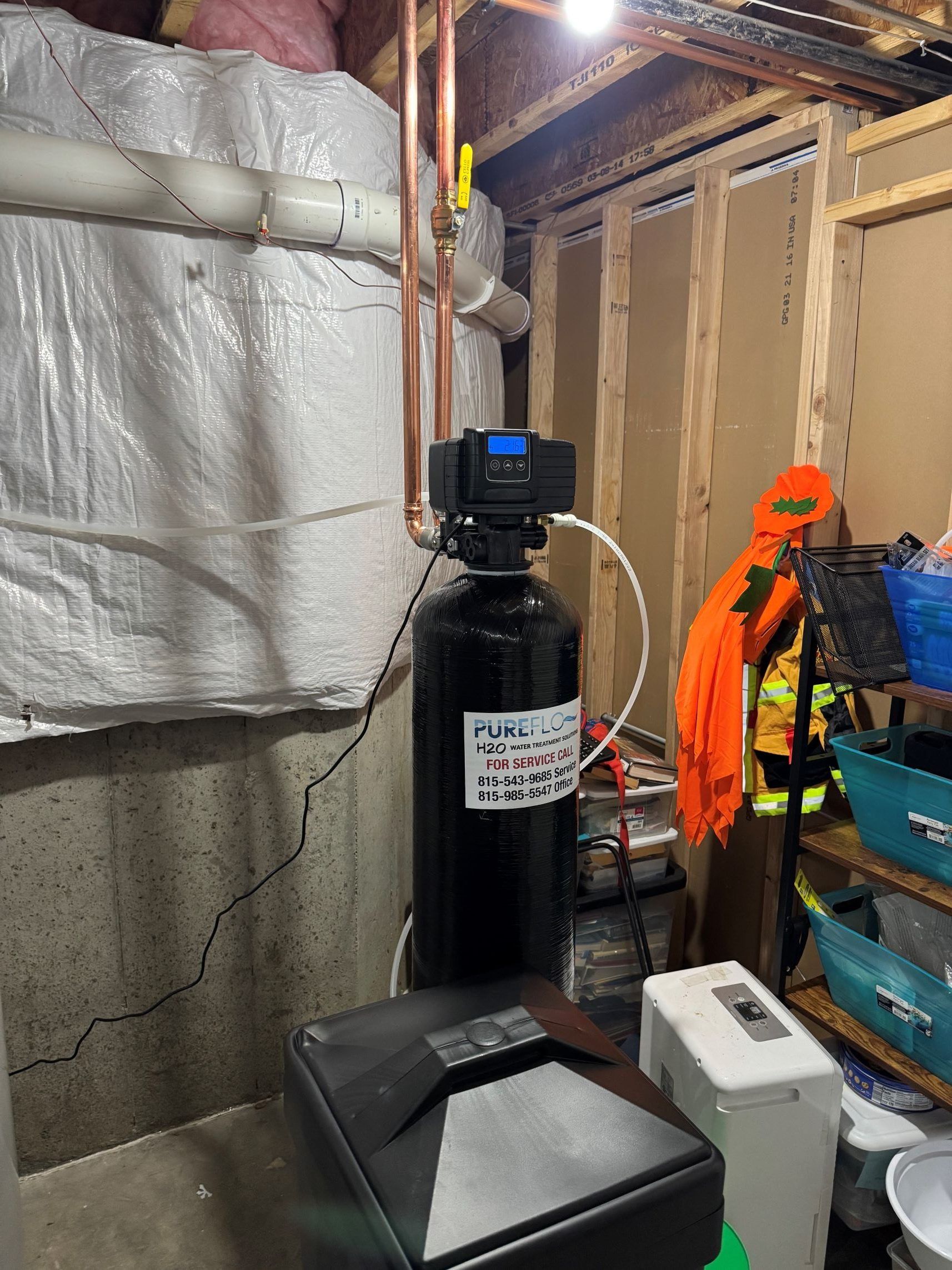 Water softener in a basement, with copper pipes and salt tank.