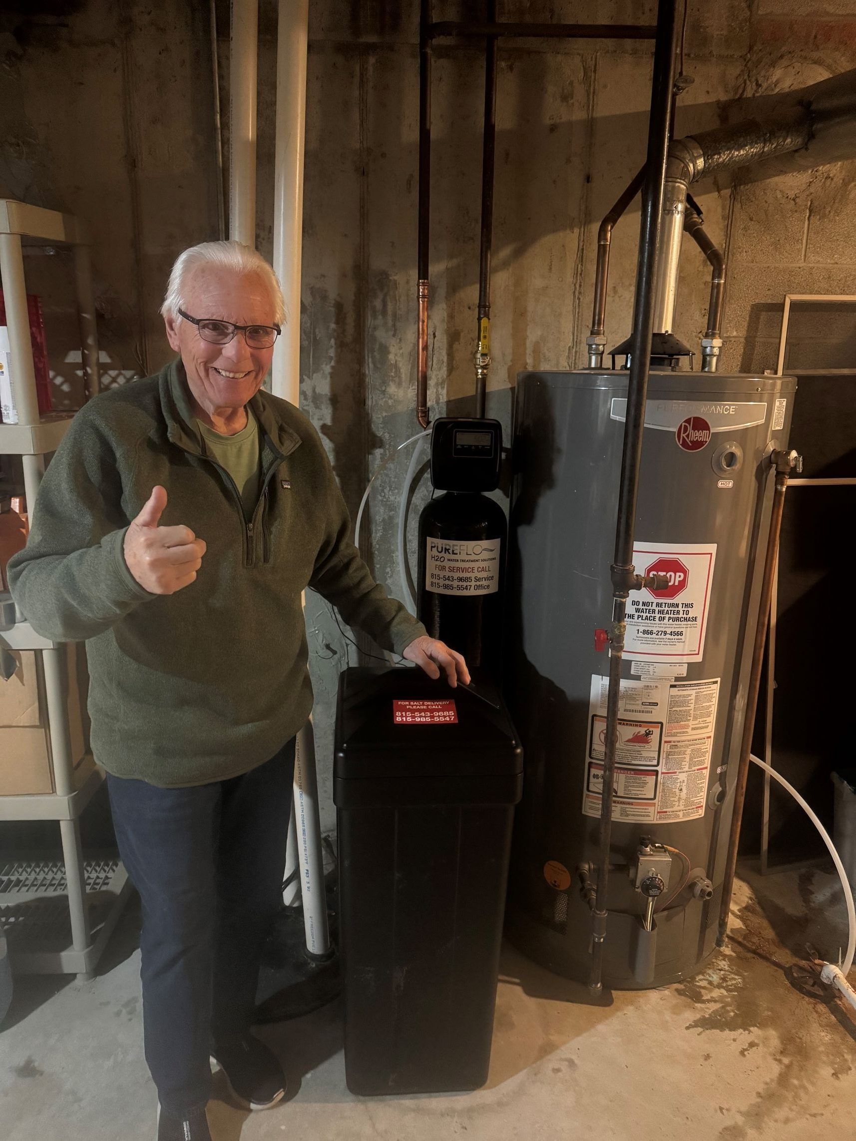 Man gives thumbs up next to a water softener and water heater in a basement.