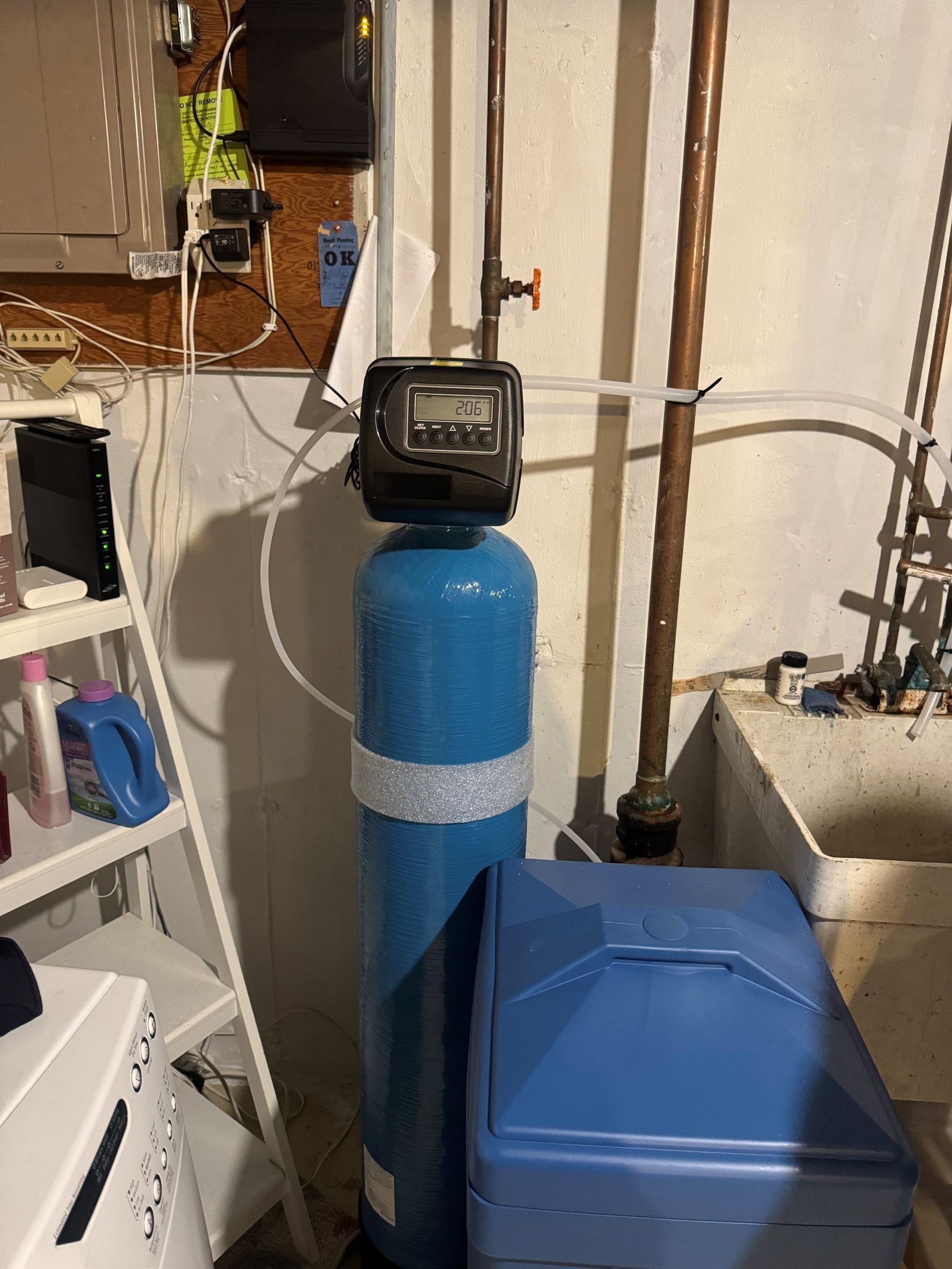 Water softener system in a basement setting with blue tank and control panel.
