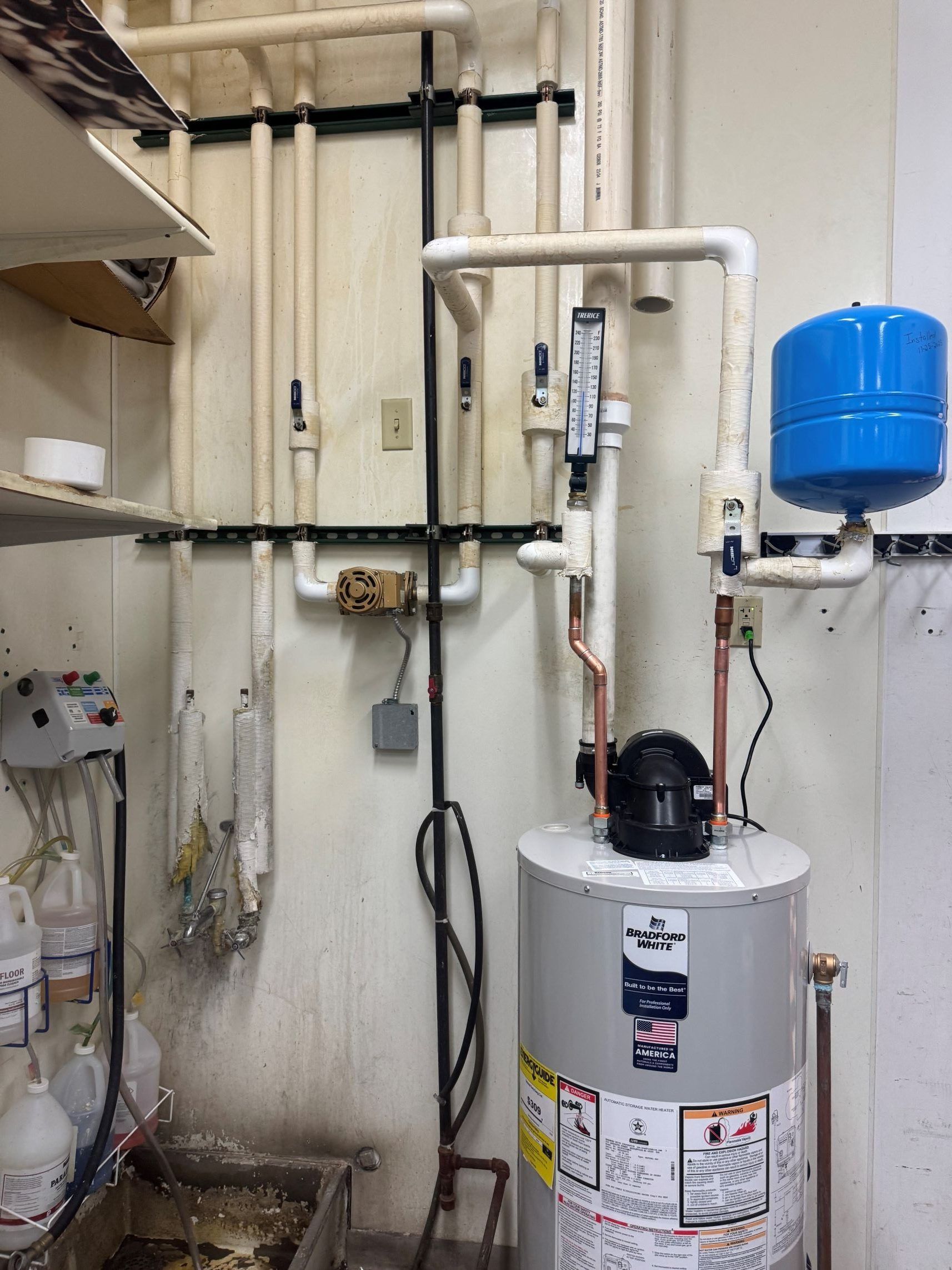A water heater and plumbing pipes are installed against a wall in a utility room.