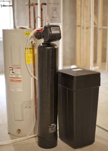 Water softener and tank next to a water heater in a basement.