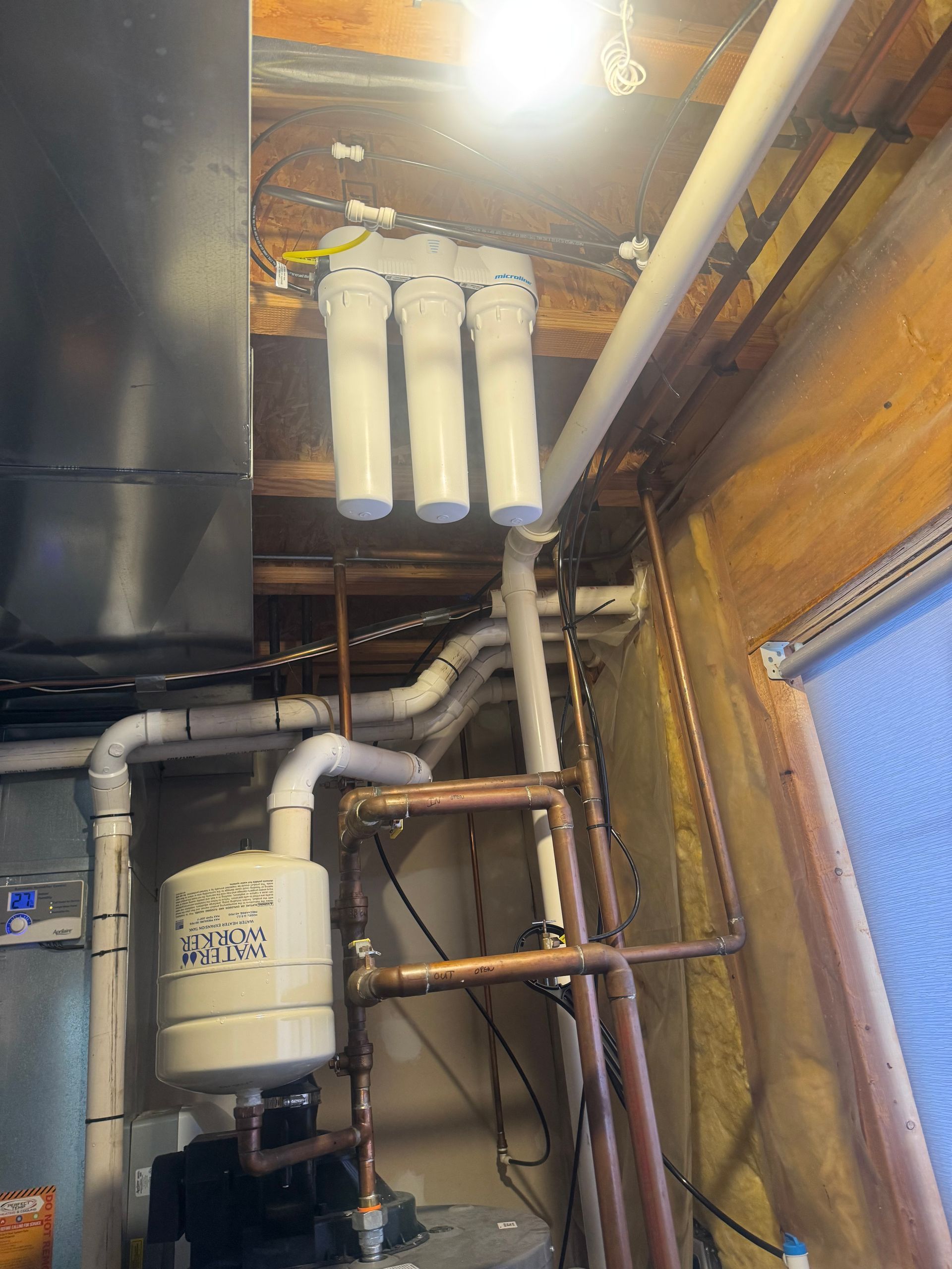 Water filtration system installed on a ceiling, with white filters, pipes, and other plumbing components.