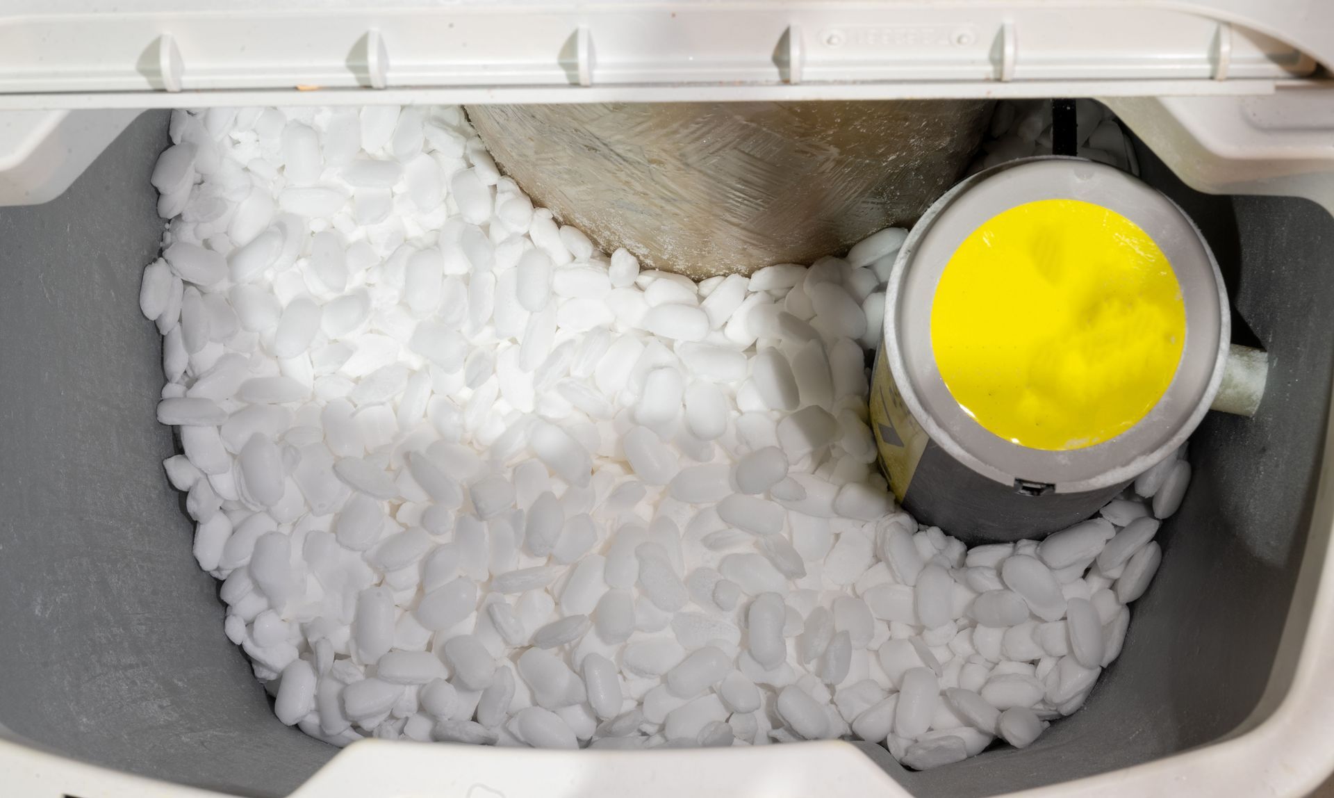 White salt pellets fill a water softener's tank. A yellow-filled cylinder is visible.