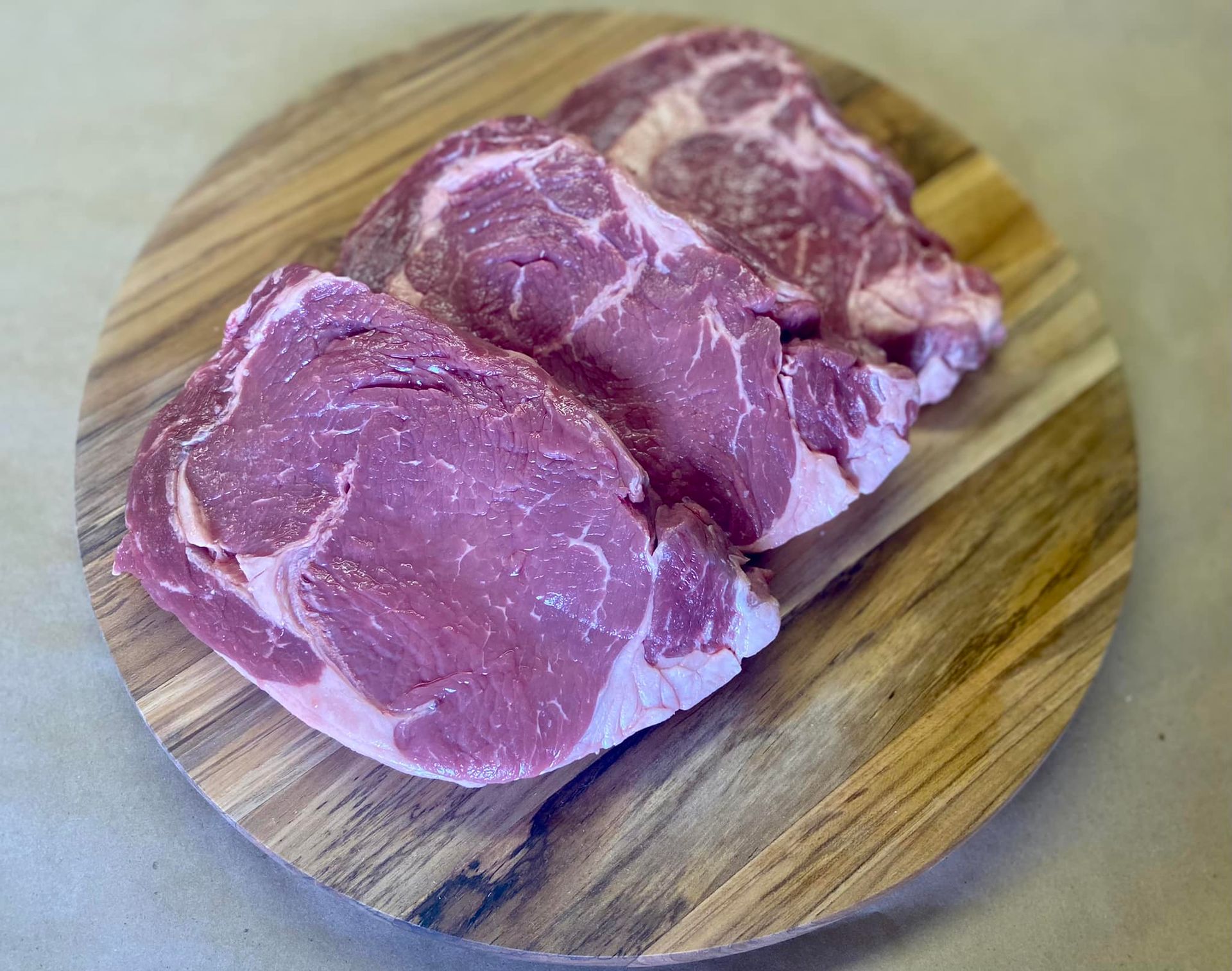 Three raw steaks are sitting on a wooden cutting board.