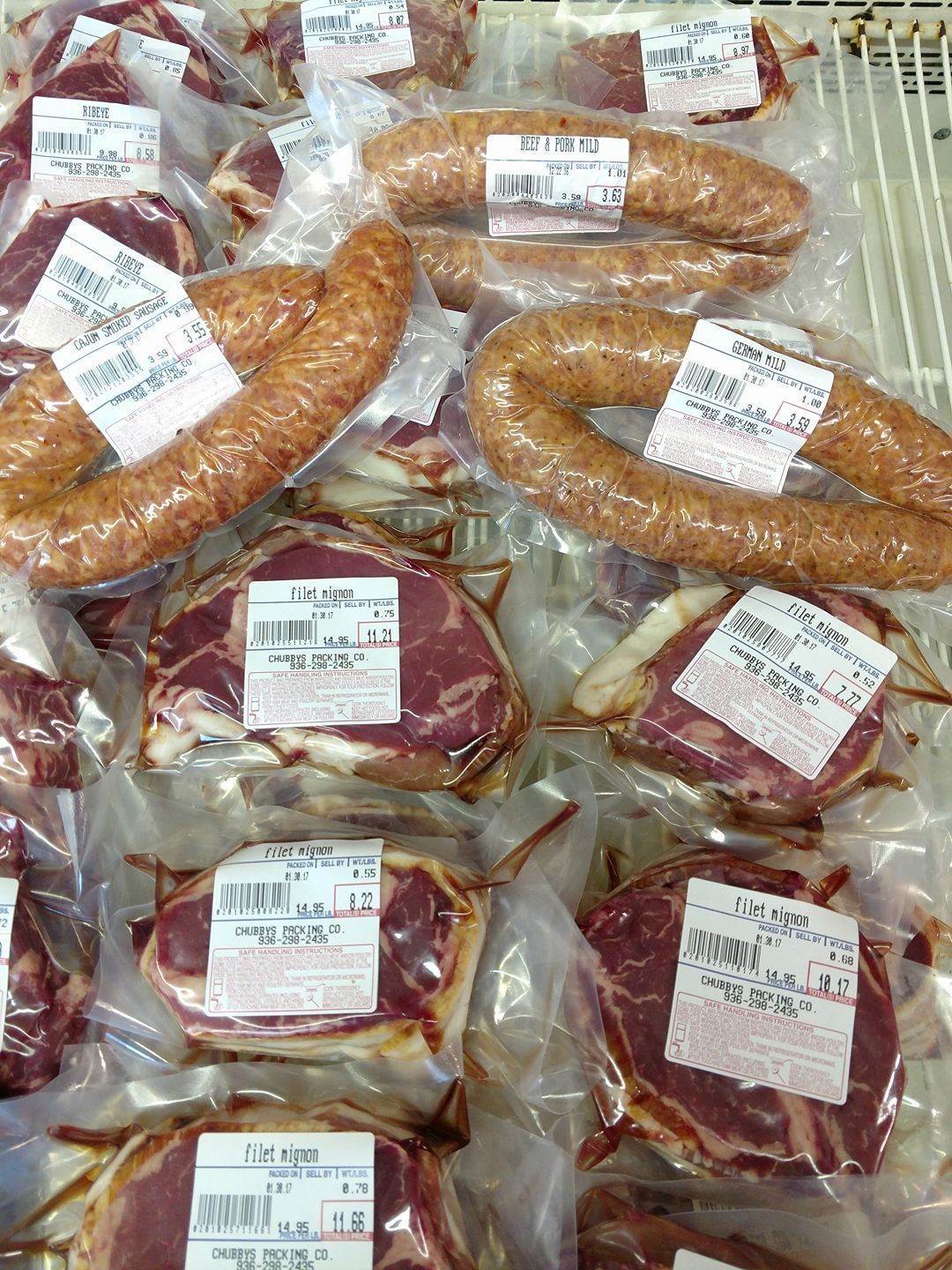 A variety of meats and sausages are sitting on top of each other on a shelf.