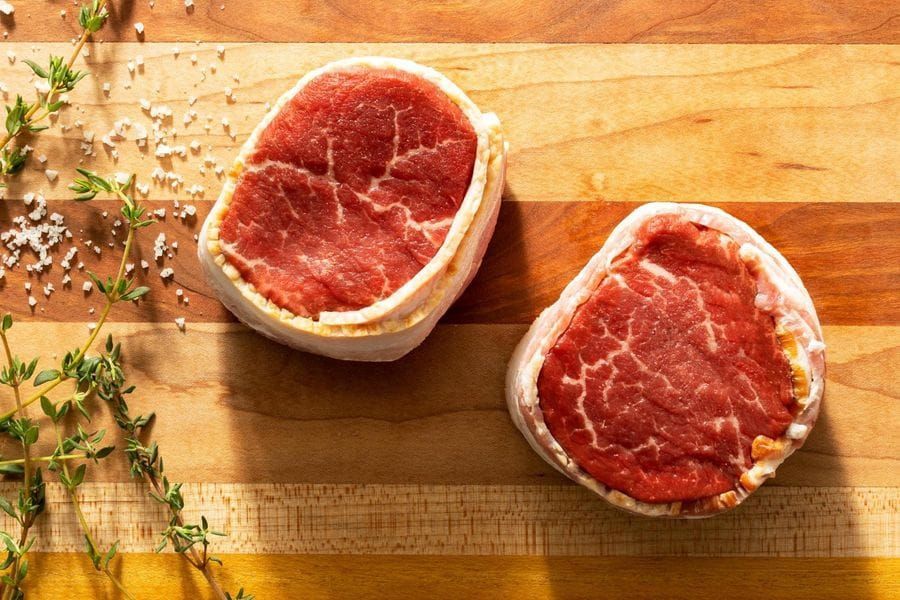 Two pieces of meat are sitting on a wooden cutting board.