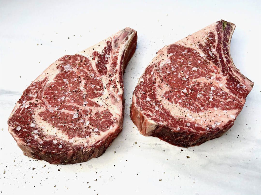 Two raw steaks are sitting on a white surface.