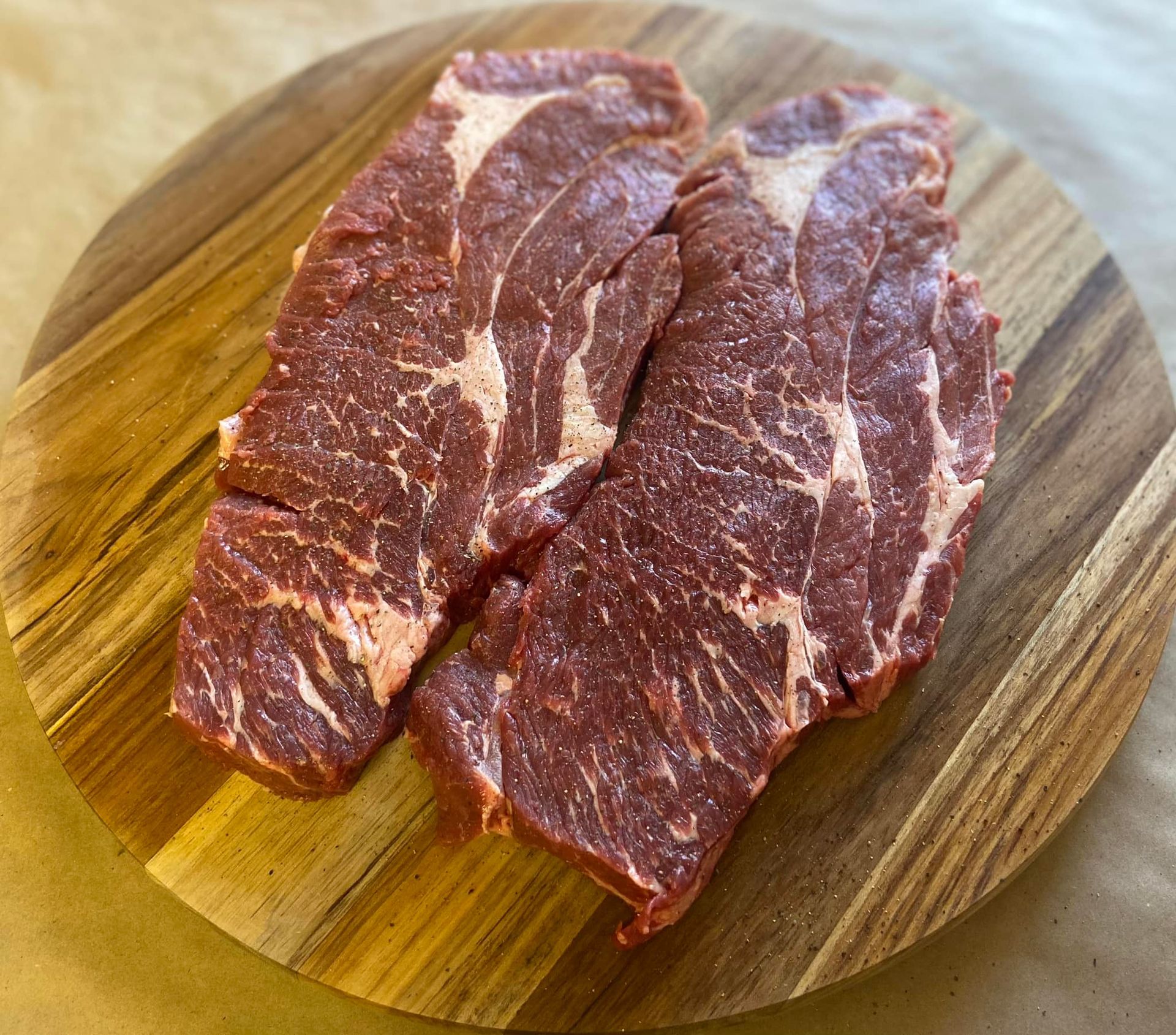 Two steaks are sitting on a wooden cutting board.