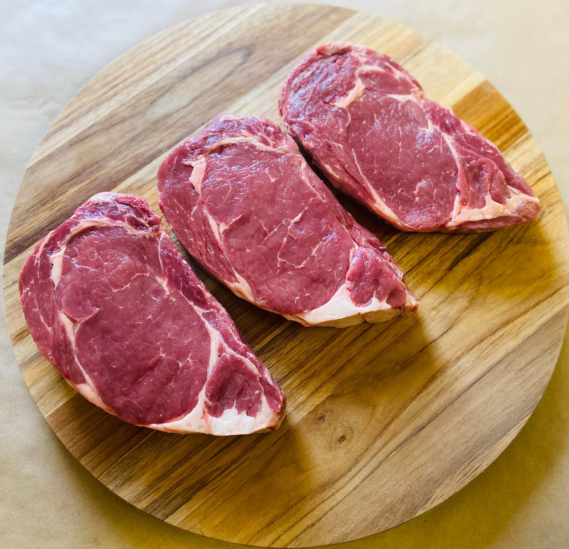 Three raw steaks are sitting on a wooden cutting board.