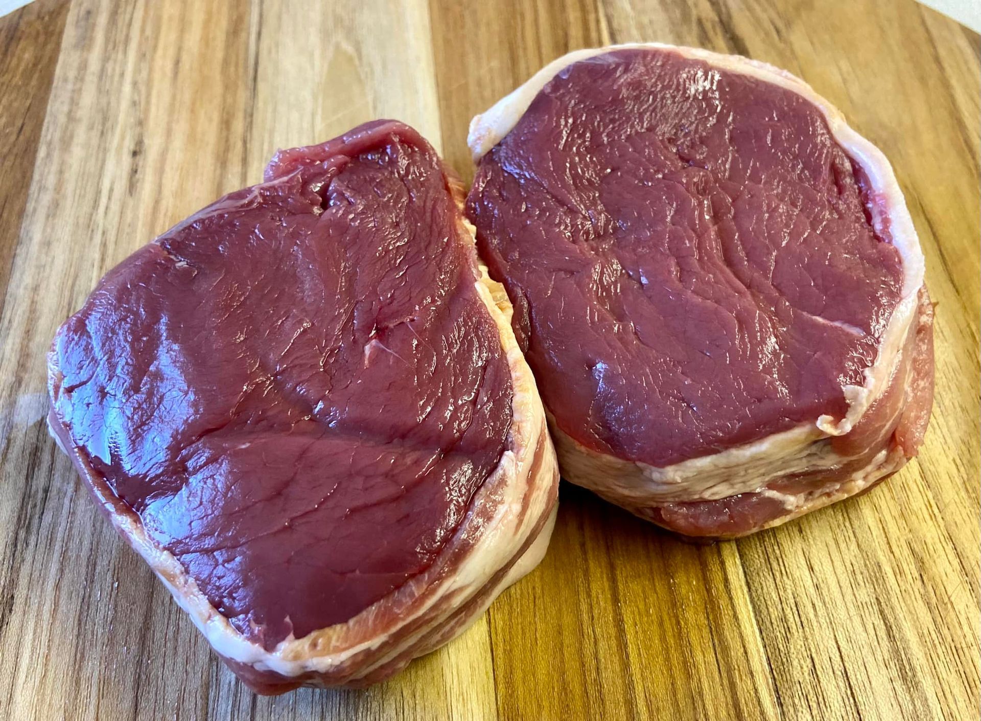 Two steaks wrapped in bacon are sitting on a wooden cutting board.