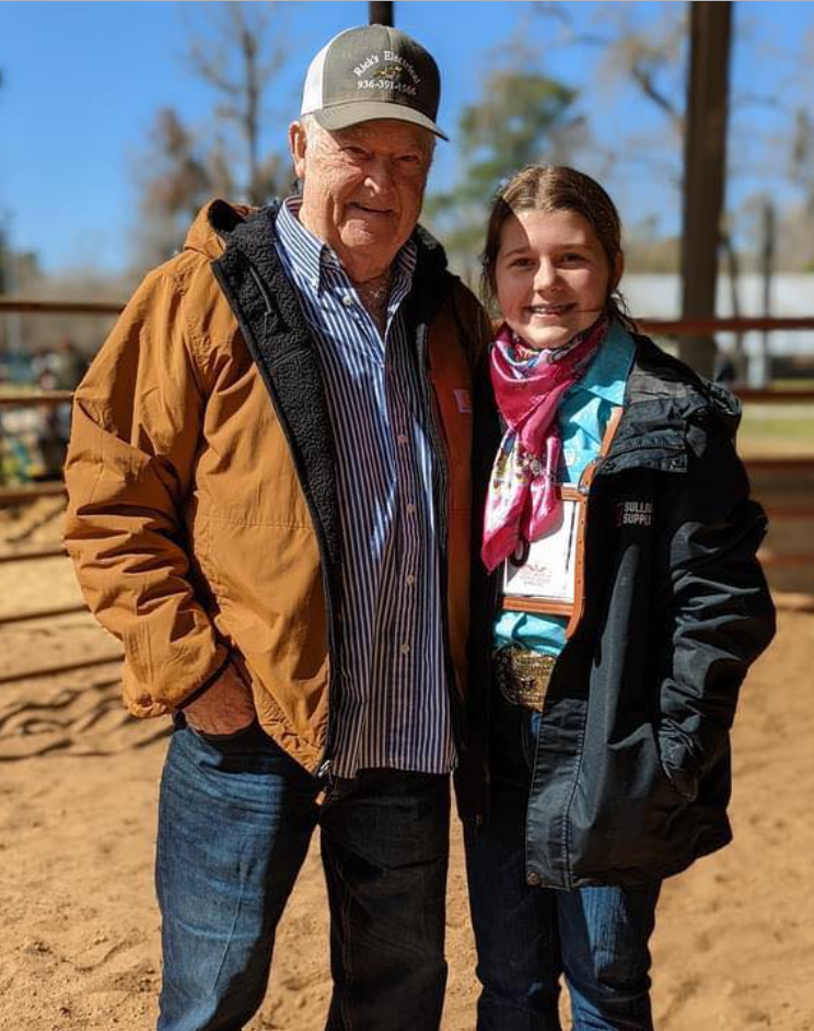 A man and a girl are standing next to each other in a dirt field.