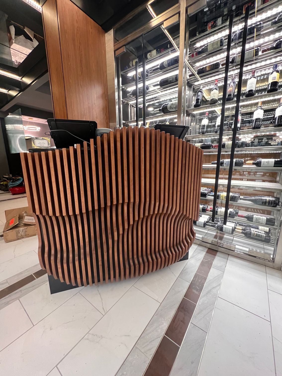 A wooden counter in front of a wine cellar filled with bottles of wine.