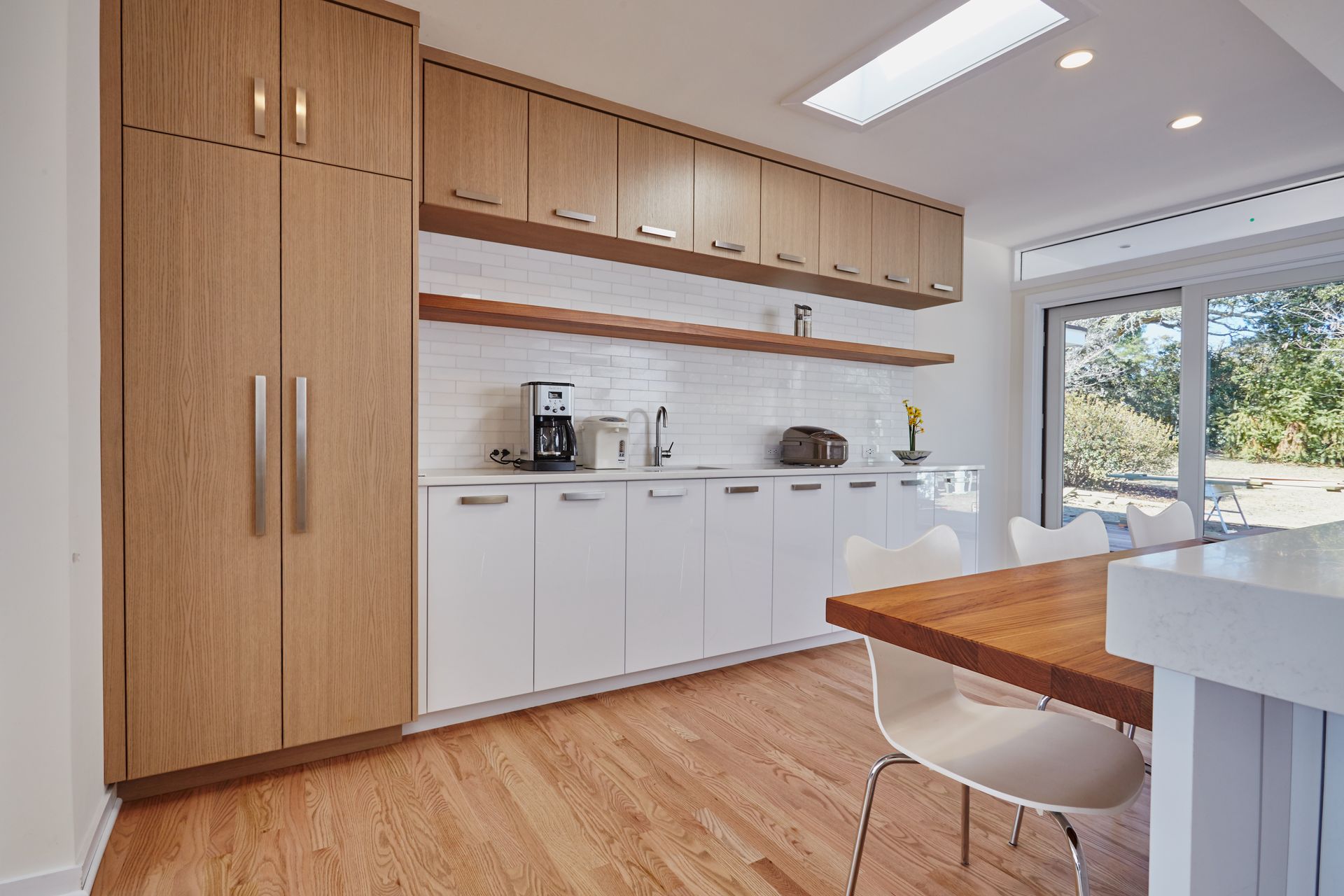 Modern kitchen with wooden cabinets, white countertops, and a wooden dining table. The space features a bright, airy feel with natural light.