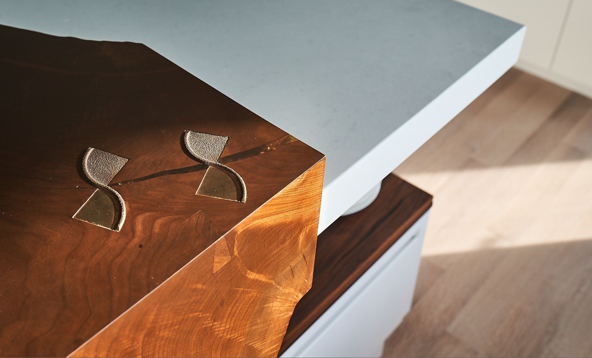 Two abstract earrings rest on a dark wooden surface next to a white, flat tabletop.