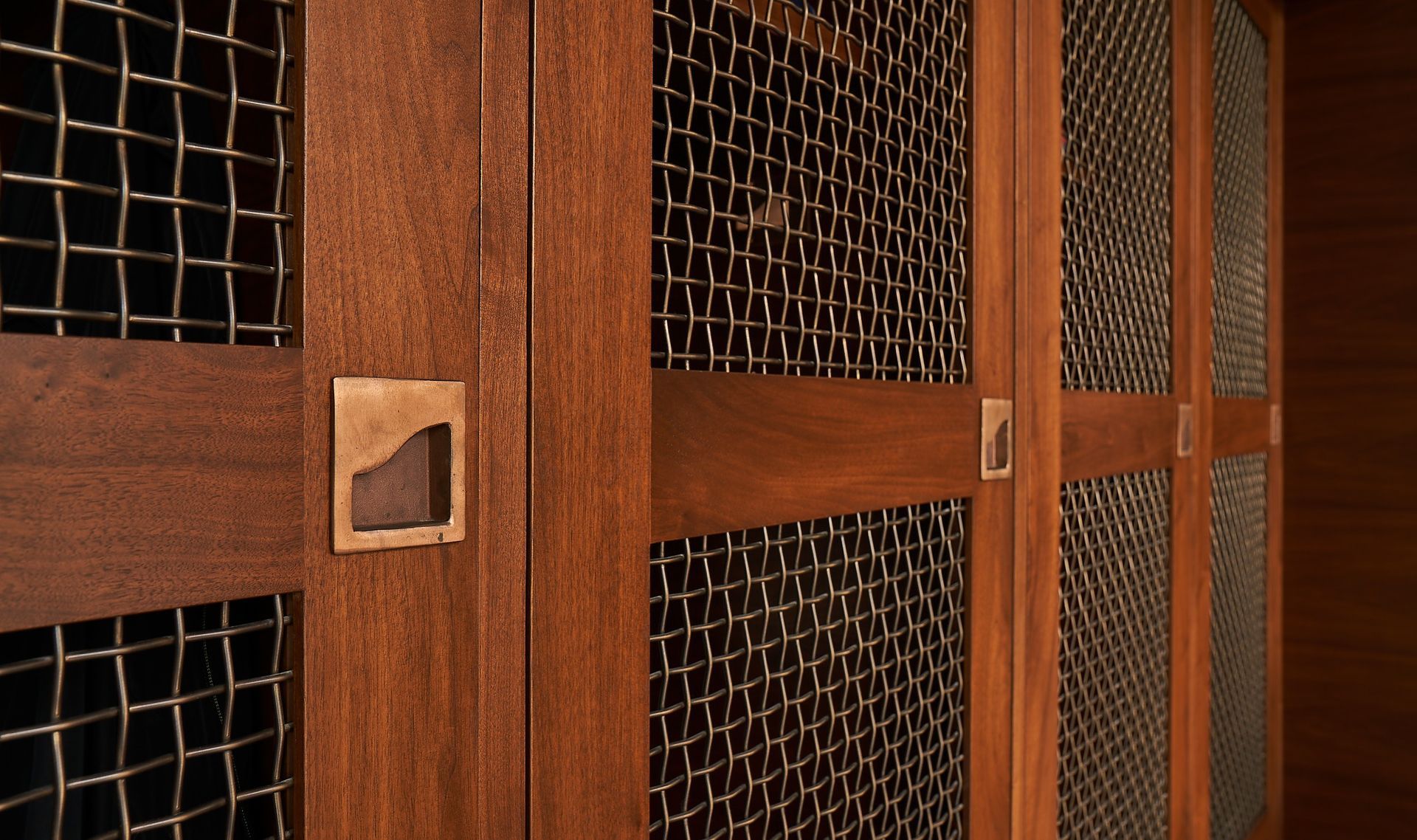 Wooden cabinet doors with metal mesh panels, bronze handles, and a dark wood finish.