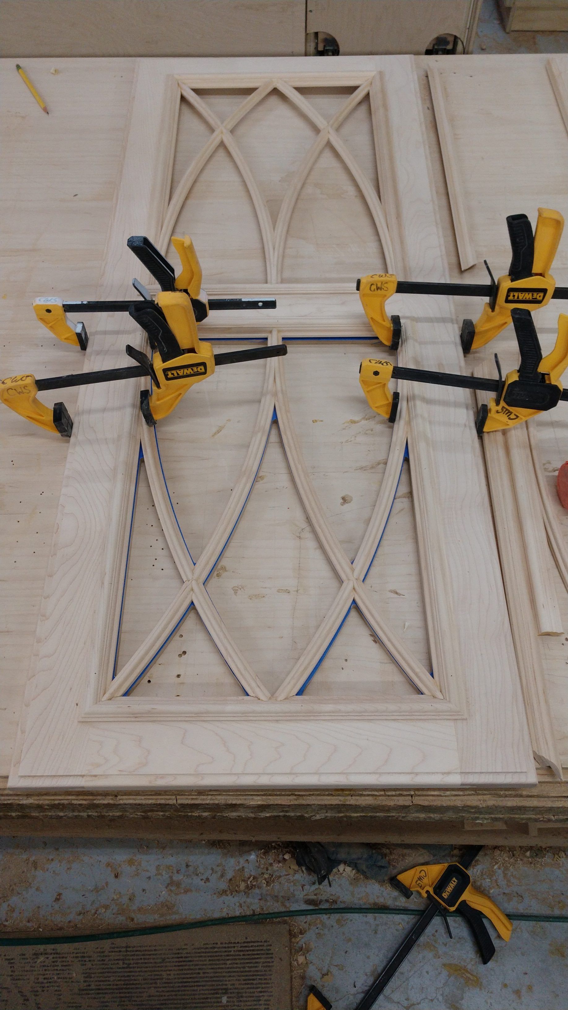 Wooden cabinet door being assembled with multiple clamps, showing an arched design in progress.