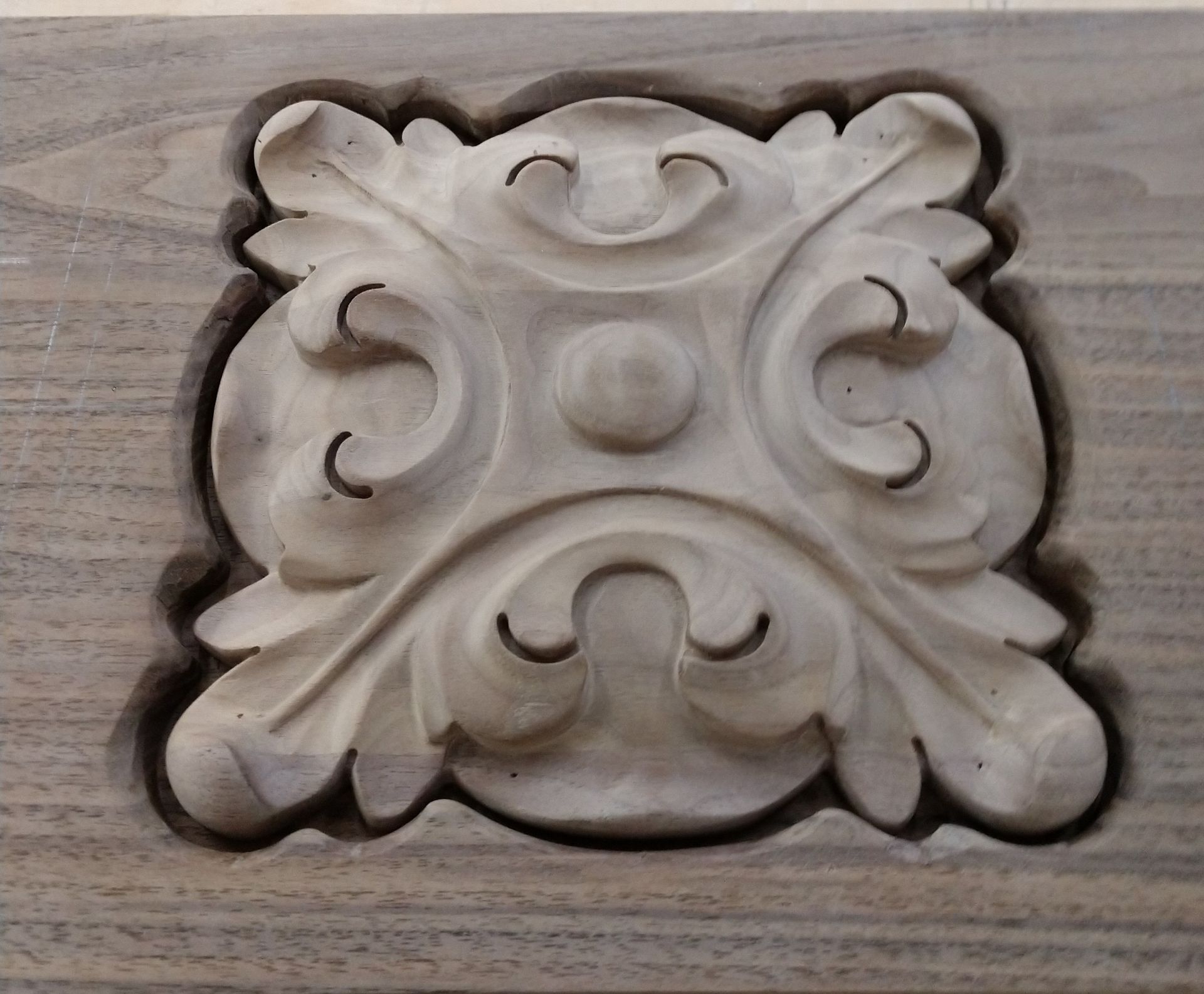 Wooden, carved decorative floral design in a recessed square on a wooden surface.