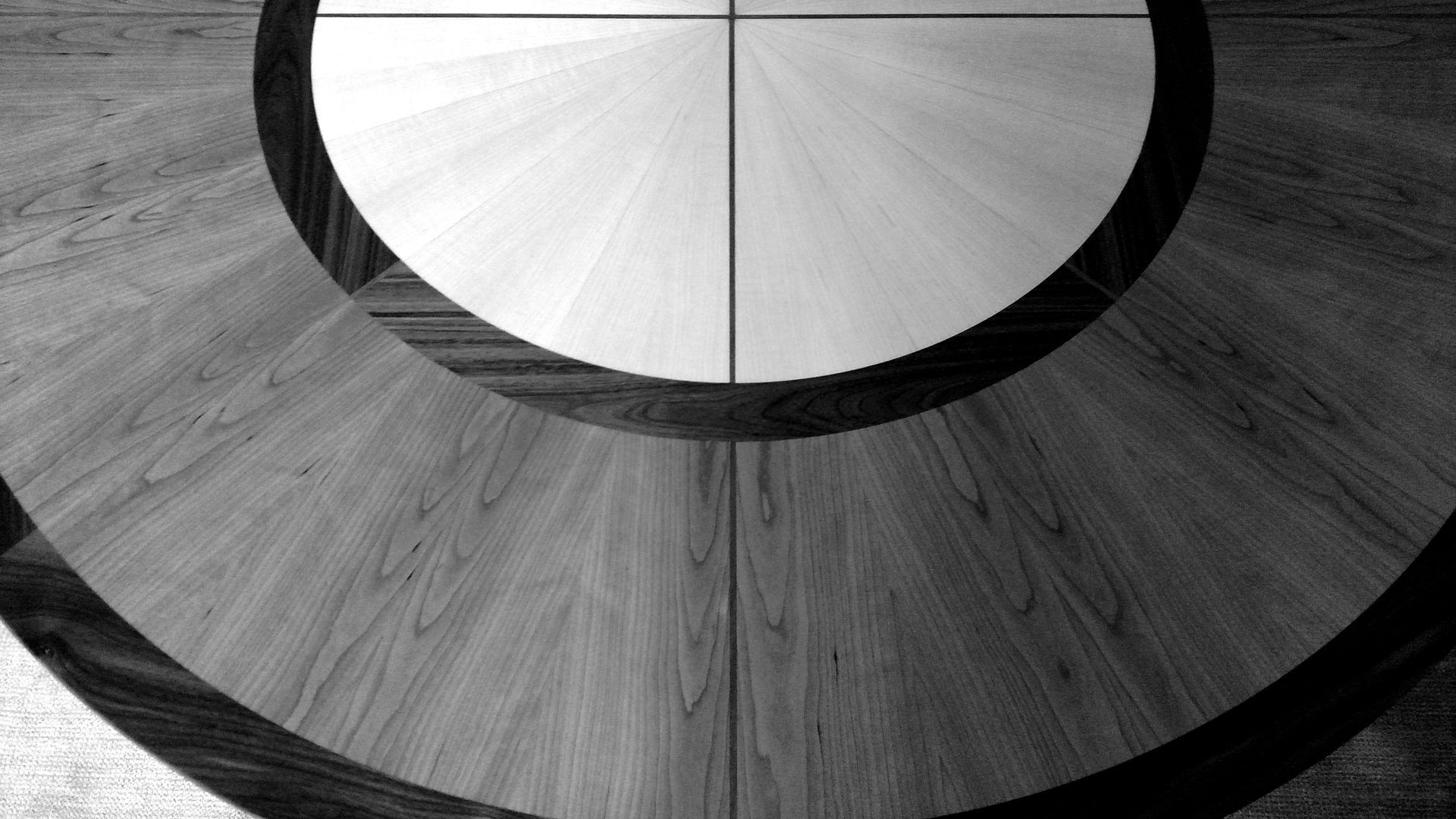 Black and white close-up of wooden flooring with concentric circles and a central quadrant pattern.