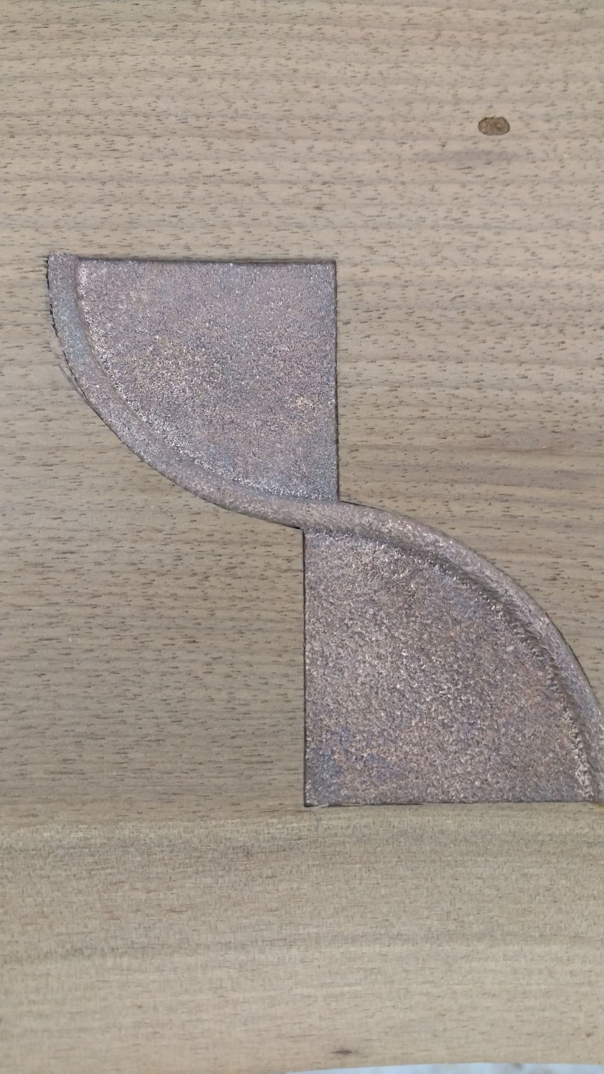 Two connected, textured, copper-colored, quarter-circle shapes inset into a light wood surface.