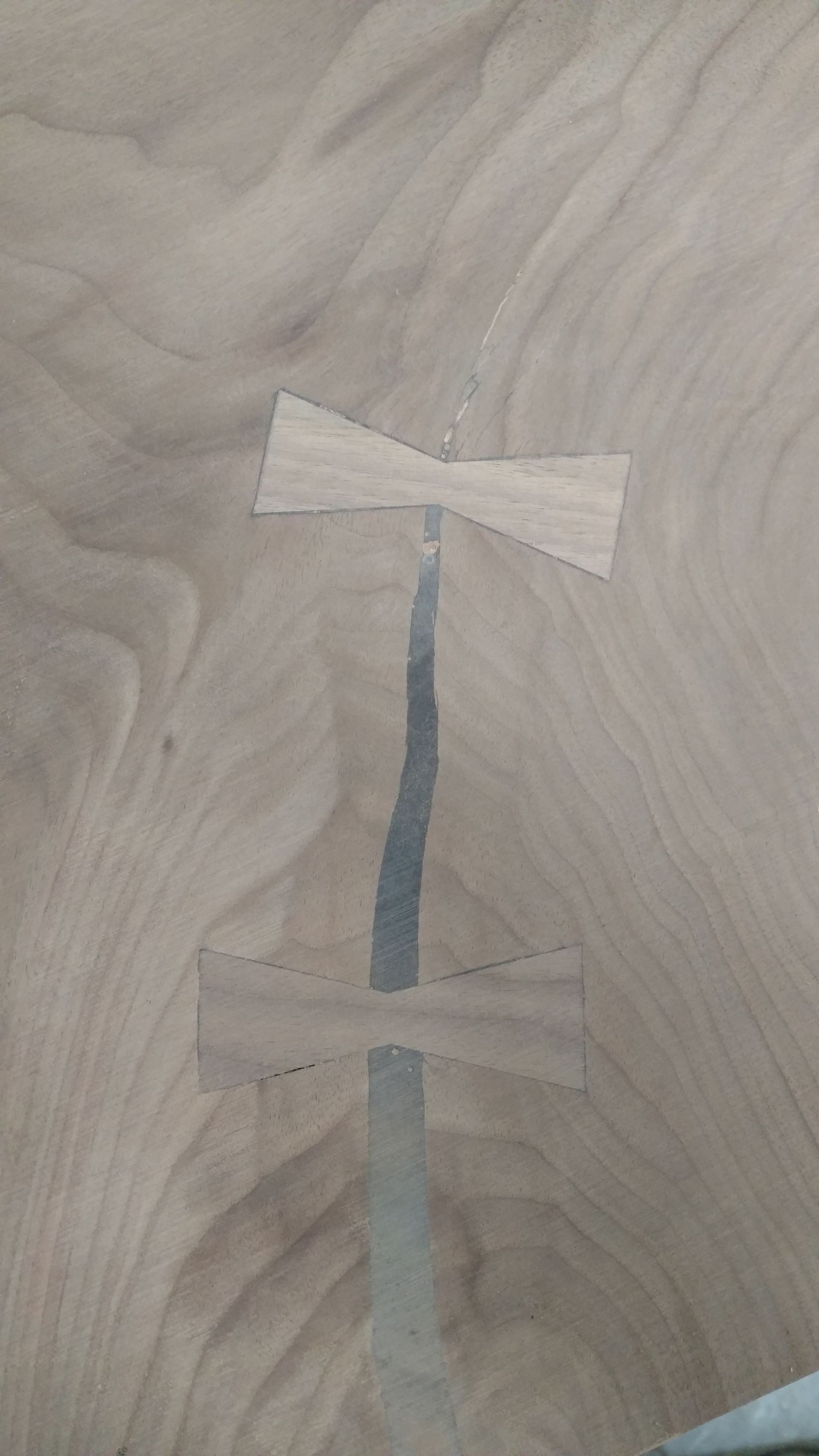 Two wooden bow tie inlays reinforcing a long crack in a light-colored wood surface.